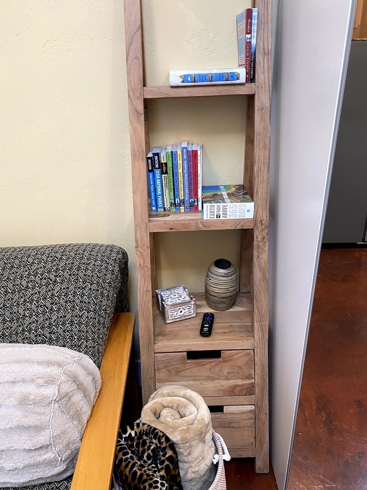 A bookshelf with books, a remote control, a decorative vase, and a patterned pillow on a couch.