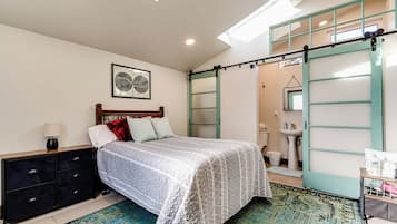 Un dormitorio con cama, cómoda, ventana y baño con lavabo y espejo.