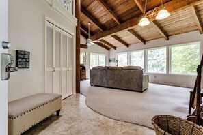 Ein geräumiger Raum mit hoher Decke, großem Fenster, einer Couch, einer Bank und einem Deckenventilator.