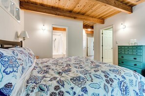 Ein Schlafzimmer mit einem großen Bett, einer Holzbalkendecke, einem Schmuckkästchen und einer Tür zu einem weiteren Raum.