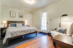 Un dormitorio con cama, mesitas de noche, una silla, una lámpara y una puerta.