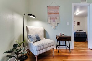 Una habitación con un sillón a rayas, una mesita pequeña, un tapiz colgado y una lámpara de pie.