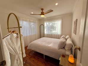 Ein Schlafzimmer mit einem Bett, einem Deckenventilator, einem Nachttisch mit Lampe und Holzboden.