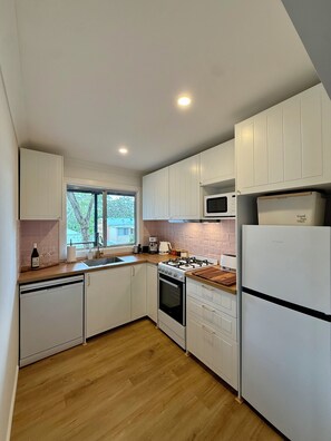Eine moderne Küche mit weißen Schränken, einer eingebauten Mikrowelle, einem Gasherd und einem Kühlschrank.