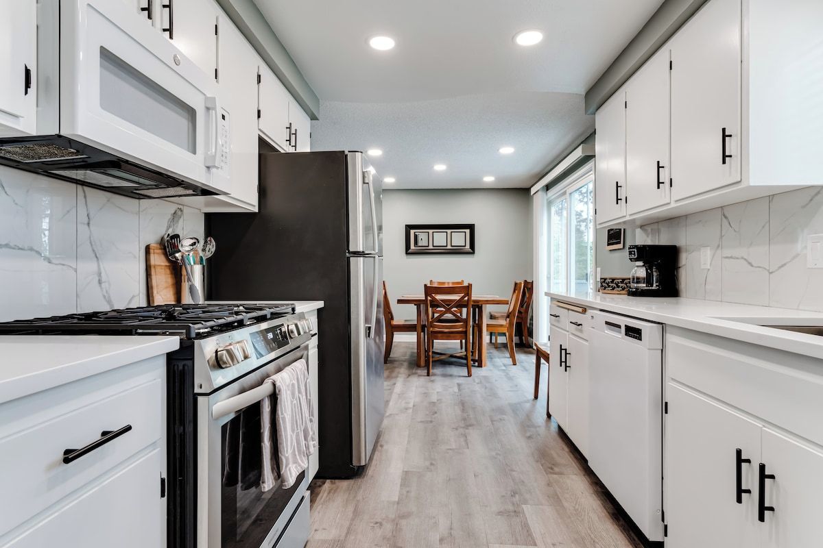 A modern kitchen with white cabinetry, a built-in oven, and a dining area with a wooden table and chairs.