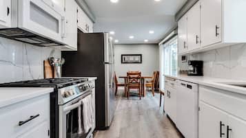 A modern kitchen with white cabinetry, a built-in oven, and a dining area with a wooden table and chairs.