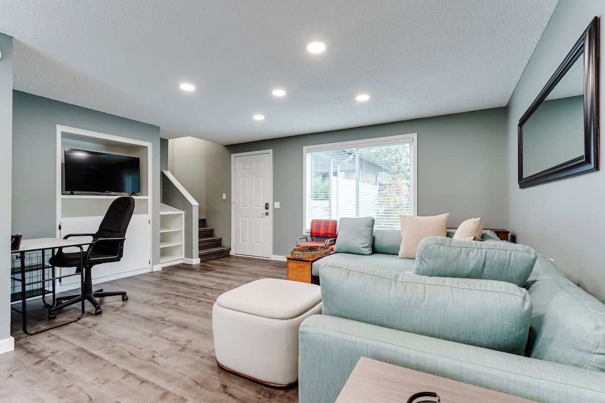 Un salon avec un canapé, un pouf et un téléviseur fixé au mur.