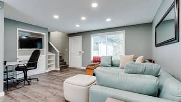 A living room with a sofa, ottoman, and a TV mounted on the wall.