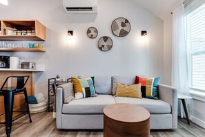 A modern living room with a grey sofa, a round wooden coffee table, and wall-mounted light fixtures. - Dog-Friendly Studio w/ Patio & Parking, Walk to (Eugene)