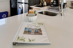 A kitchen counter with a white bowl containing a chocolate bar, a welcome sign, and a kitchen sink. - Dog-Friendly Studio w/ Patio & Parking, Walk to (Eugene)