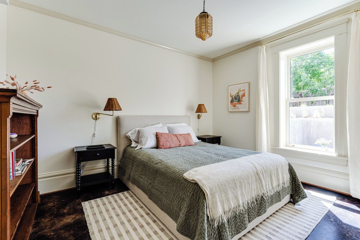 A bedroom with a bed, bedside tables, a lamp, a bookshelf, and a window with curtains.