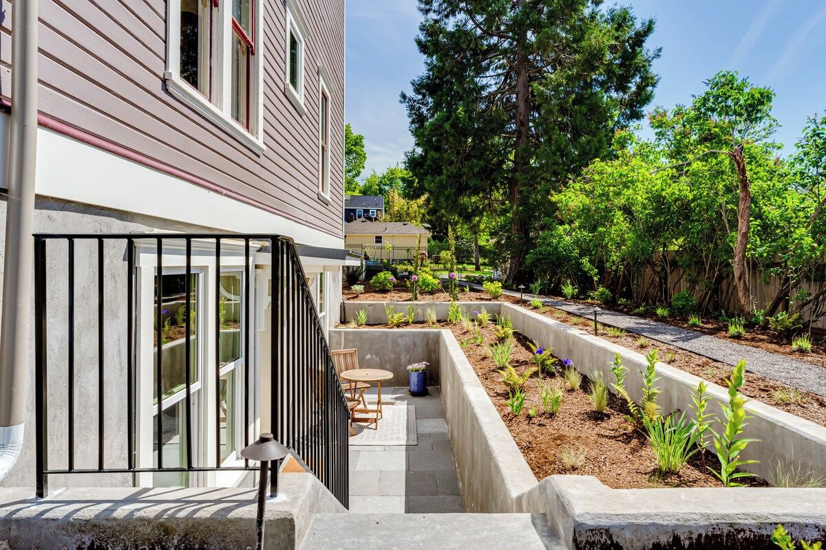A residential property with a covered patio, outdoor seating, and a landscaped garden with various plants.