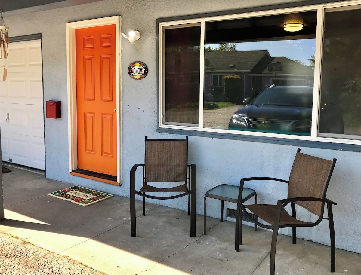 Ett hus med en orange dörr, två stolar utanför och en garageport.