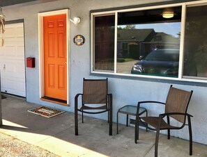 Ett hus med en orange dörr, två stolar utanför och en garageport.