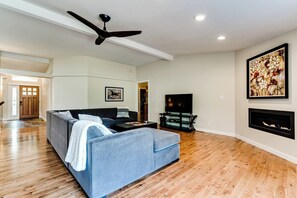A living room with a sofa, a TV, a fireplace, and a ceiling fan. - Secluded Garden Retreat w/ Game Room & BBQ Patio (Eugene)