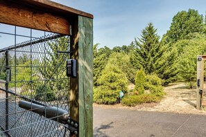 A gated entrance with a wooden post, a chain-link fence, and a pathway leading into a wooded area. - Secluded Garden Retreat w/ Game Room & BBQ Patio (Eugene)