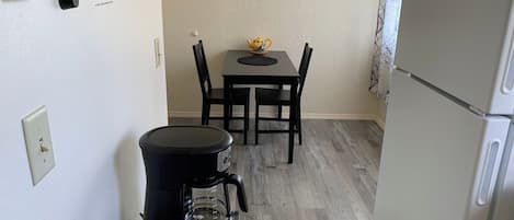 A compact kitchen with a coffee maker, a kettle, a refrigerator, and a framed picture on the wall.