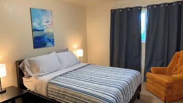Quarto com cama, cadeira, quadro e janela com cortinas.