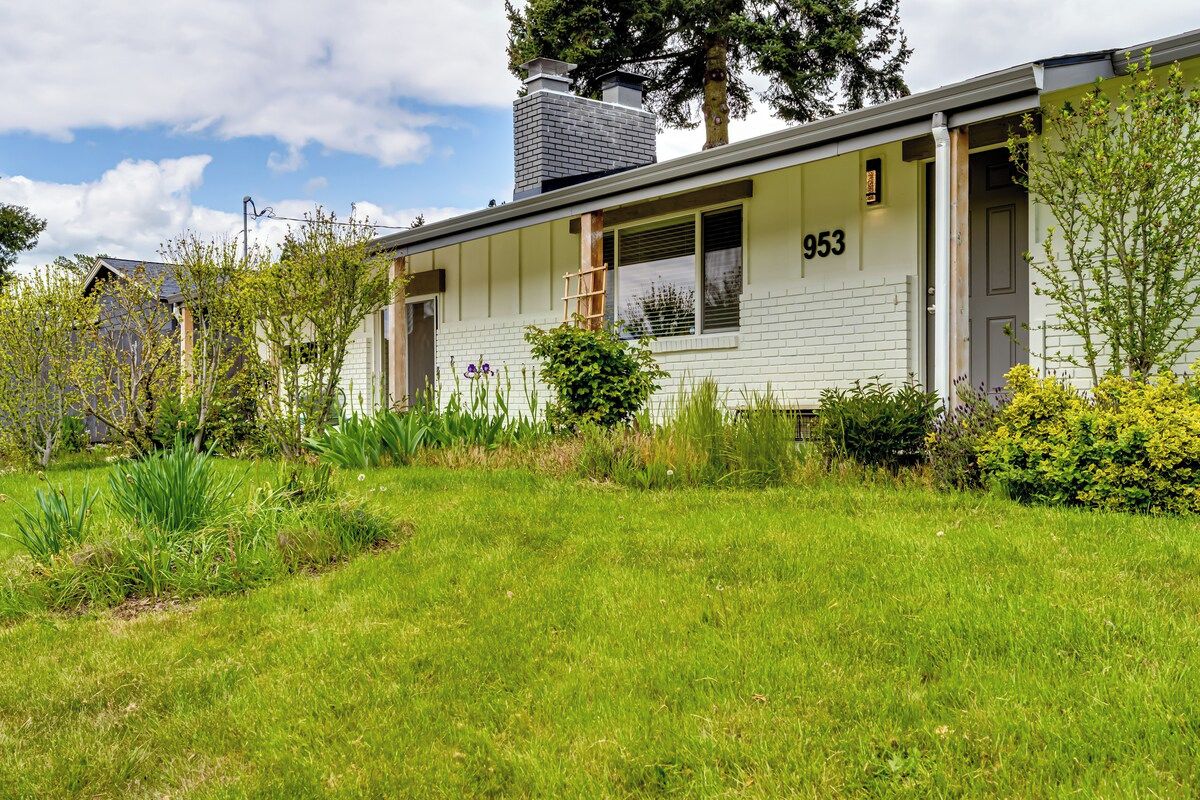 Een gelijkvloers huis met het nummer '953' aan de zijkant, omgeven door een verzorgd gazon en diverse planten.