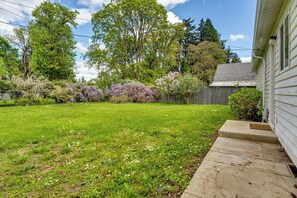 Un jardin arrière d’une maison, avec une pelouse, une clôture en bois et divers arbustes à fleurs.