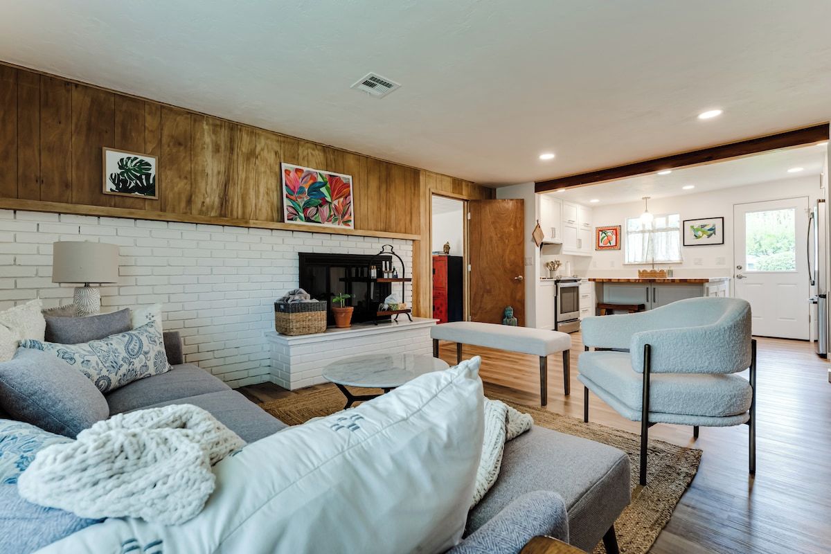 A modern living room with a fireplace, a sofa, a bench, and a kitchen area visible through an open door.