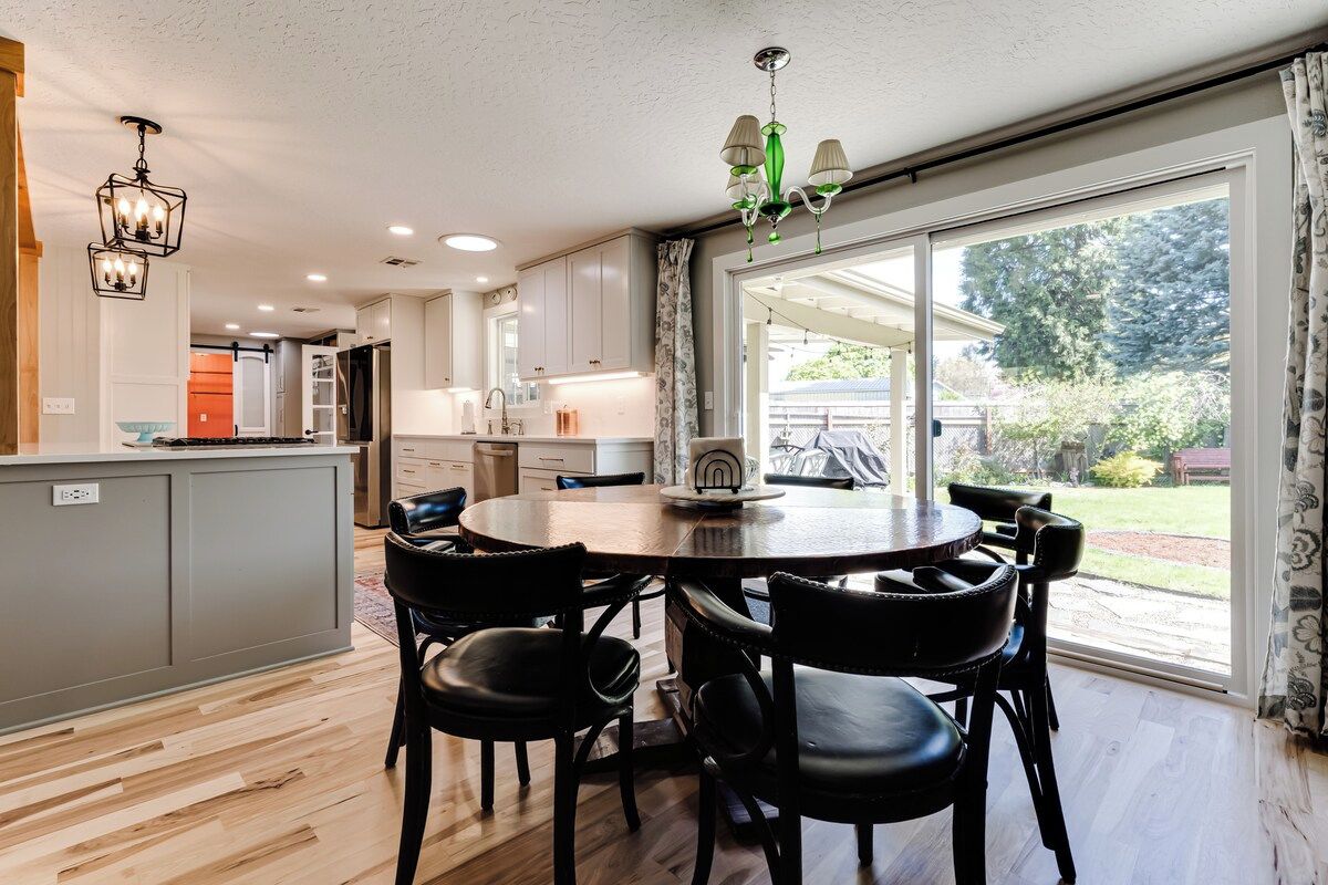 A modern kitchen with a dining area, large windows, and a view of the outdoors.
