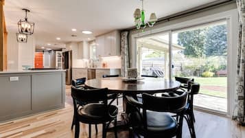 A modern kitchen with a dining area, large windows, and a view of the outdoors.