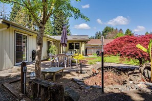 A residential property with a patio area, outdoor seating, a tree, and a garden with red foliage. - Serene Backyard Oasis w/ Free Parking & Modern (Eugene)