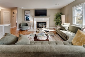 A living room with a fireplace, a sofa set, a coffee table, and a television mounted above the fireplace. - Luxury Eugene Home w/Gourmet Kitchen & Office (Eugene)