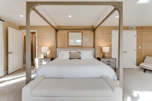 Une chambre à coucher avec un lit à baldaquin, des tables de chevet, un banc et une vue sur le couloir.