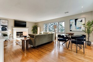 Un salon moderne avec une cheminée, un canapé, une table à manger avec des chaises et de grandes fenêtres.