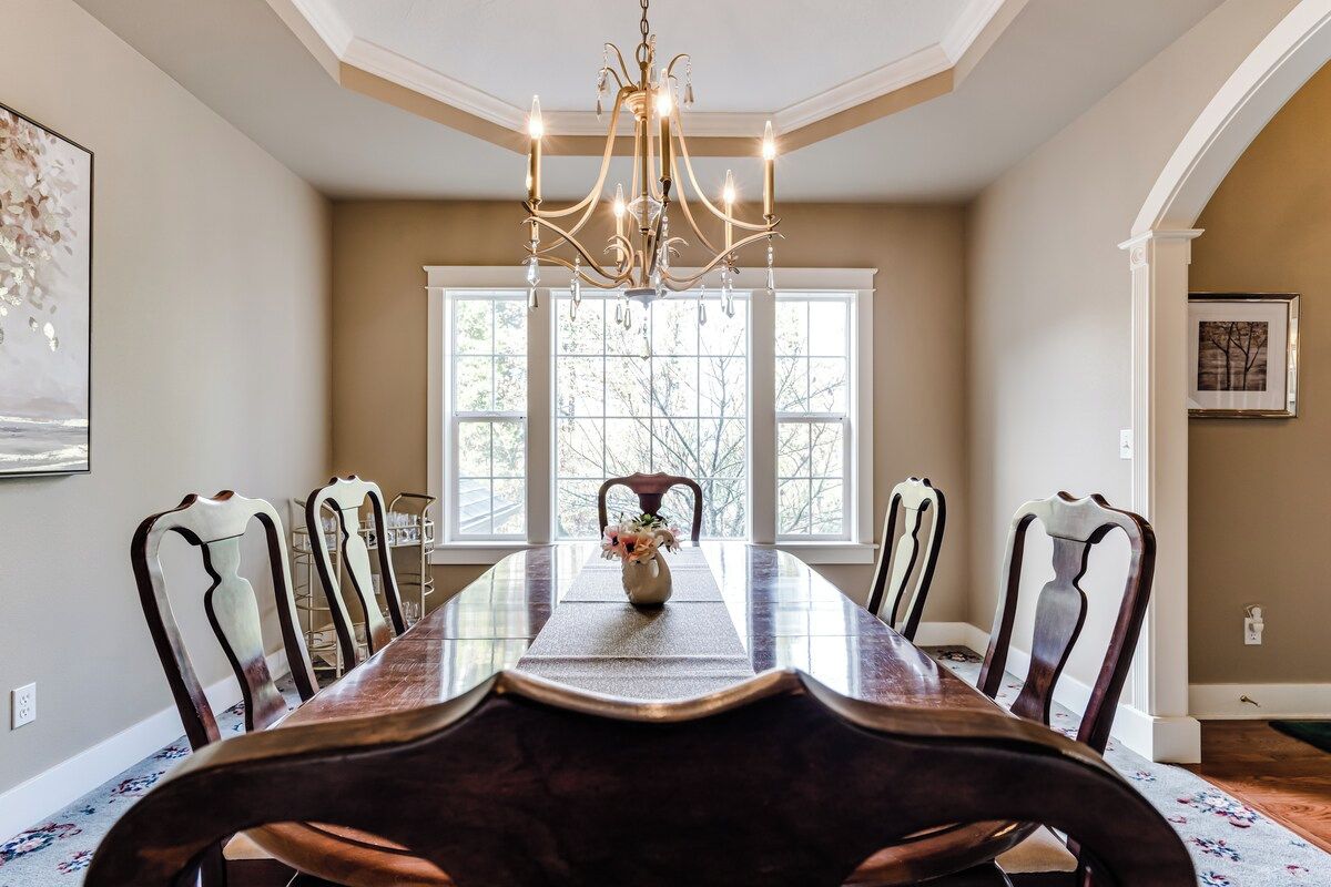 A dining room with a long table, chairs, a chandelier, and a window with a view.