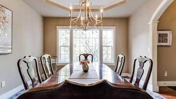 A dining room with a long table, chairs, a chandelier, and a window with a view.
