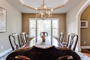 Une salle à manger avec une longue table, des chaises, un lustre et une fenêtre donnant sur un beau paysage.