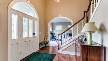 A hallway with a wooden floor, a green carpet, a staircase with a wooden railing, and a chandelier.
