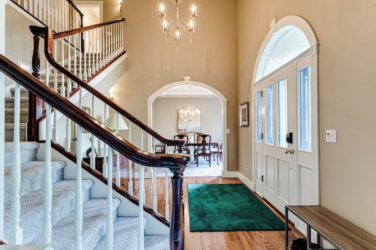 A staircase with a wooden handrail and white balusters, leading to a dining area with a chandelier.