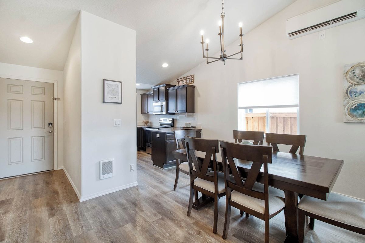 A modern kitchen with dark cabinetry, a dining area with a wooden table and chairs, and a chandelier.