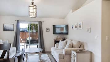 A living room with a sofa, a TV, a dining table, and a chandelier.