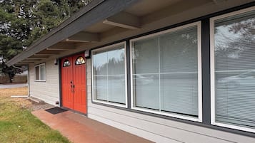 A single-story house with a red front door, large windows with blinds, and a visible front porch.