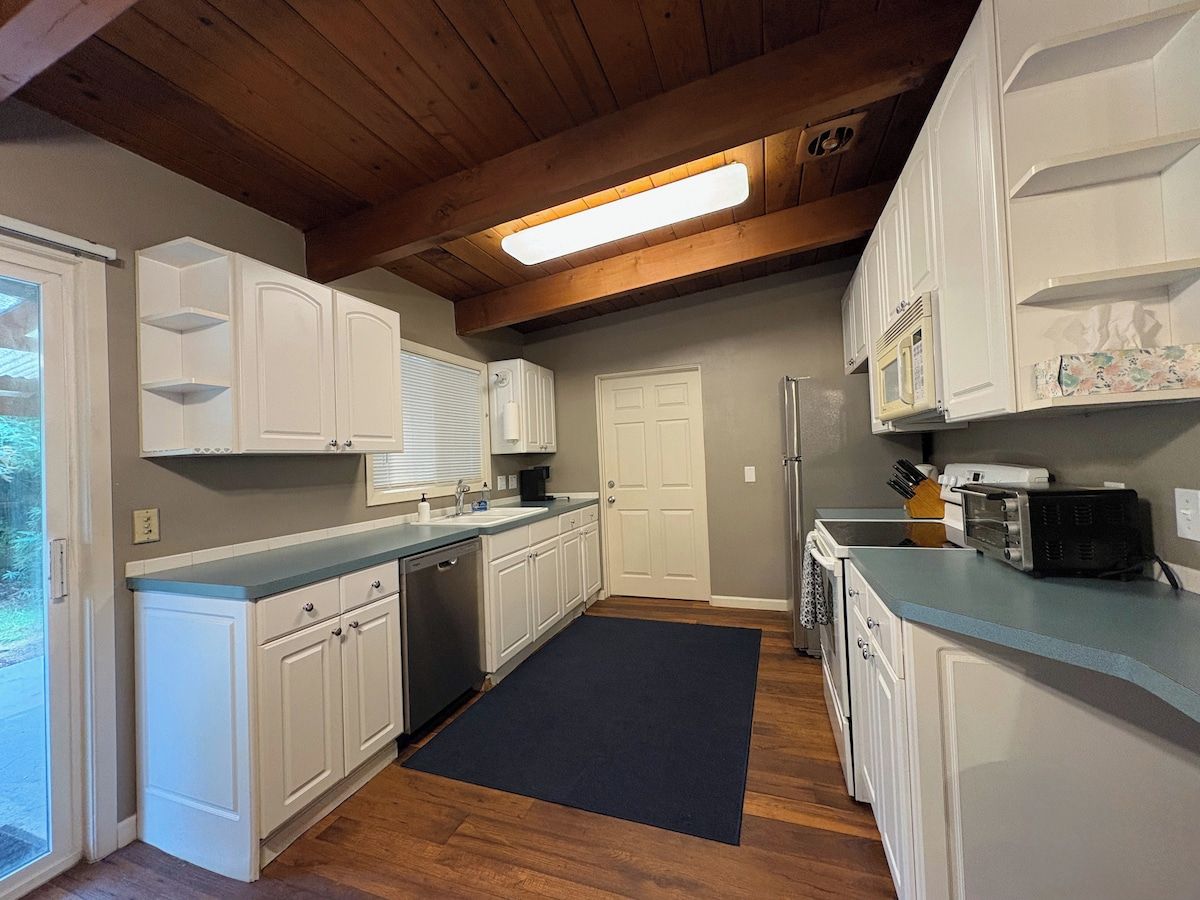 A kitchen with white cabinets, a black rug, and wooden flooring.