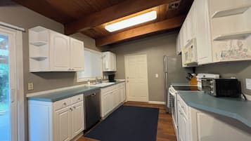 A kitchen with white cabinets, a black rug, and wooden flooring.