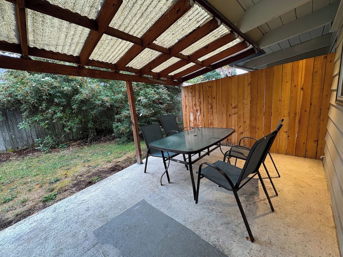 A covered patio with a table and chairs, a wooden fence, and a grassy yard.