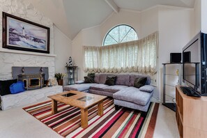 Ein Wohnzimmer mit Kamin, großem Fenster, einer Couch, einem Couchtisch und einem Fernseher.
