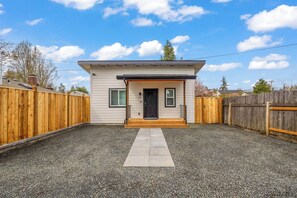 A single-story house with a front porch, a black door, and a gravel driveway. - New Home Near Hayward Field & University, Fast (Eugene)