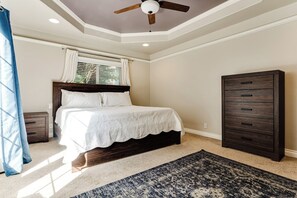 A bedroom with a bed, a ceiling fan, a window with curtains, a dresser, and a patterned rug. - Thurston Hills Retreat: Modern Home w/ Scenic (Springfield)