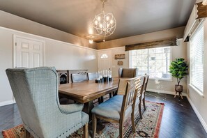 A dining area with a wooden table, upholstered chairs, a chandelier, and a window with blinds. - Thurston Hills Retreat: Modern Home w/ Scenic (Springfield)