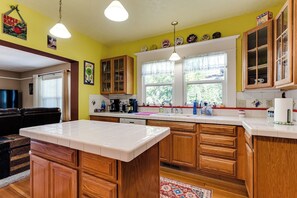 Une cuisine avec des meubles de rangement en bois, un plan de travail blanc et une fenêtre avec des rideaux.
