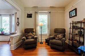 A living room with two armchairs, a floor lamp, and a bookshelf. - Historic Manor w/ Hot Tub, Walk to UO & Hayward (Eugene)
