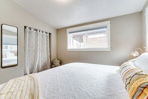 Een slaapkamer met een groot bed, een raam met zonwering, een spiegel en een bedlampje.