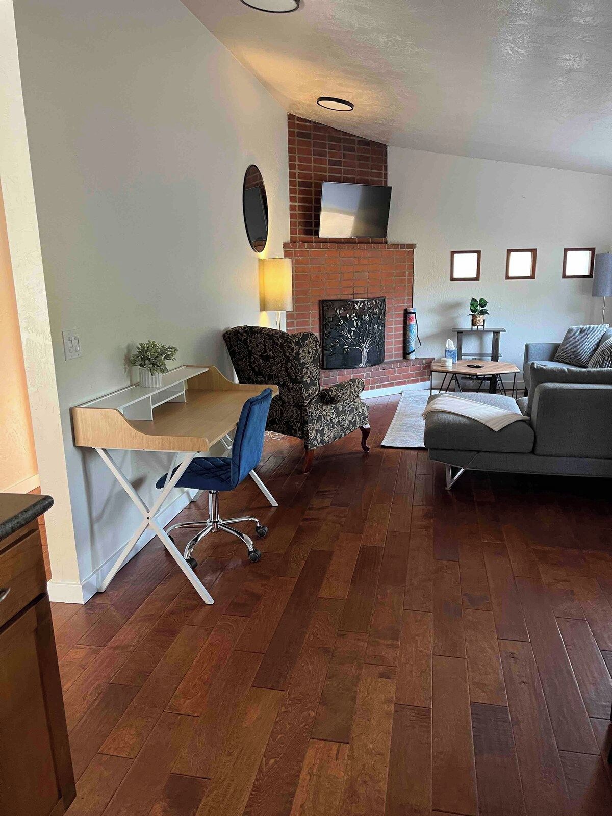 A living room with a fireplace, a sofa, a chair, a desk, and a TV.